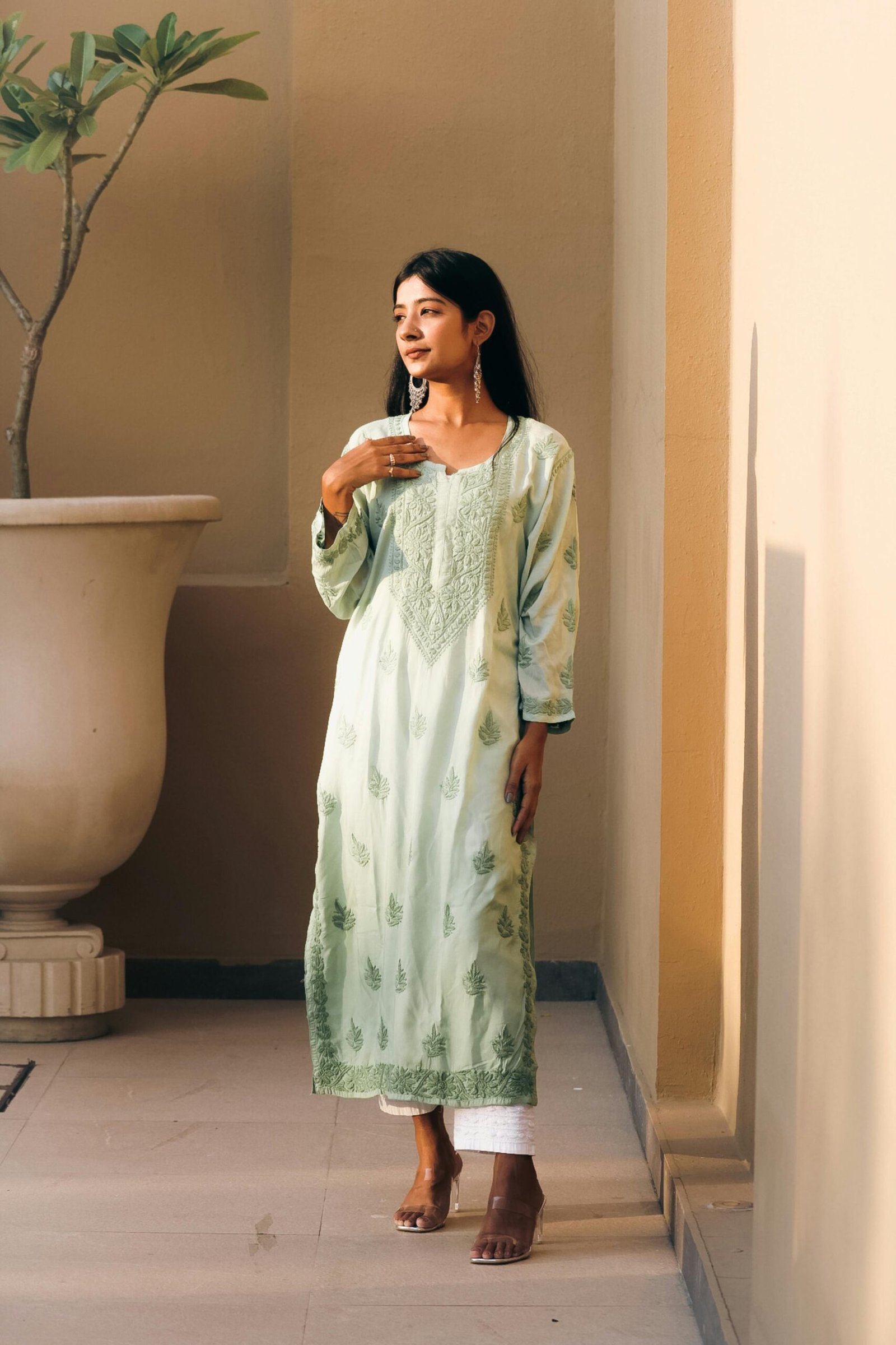 South Asian woman in traditional pistachio green chikankari kurti, enjoying a serene moment indoors.